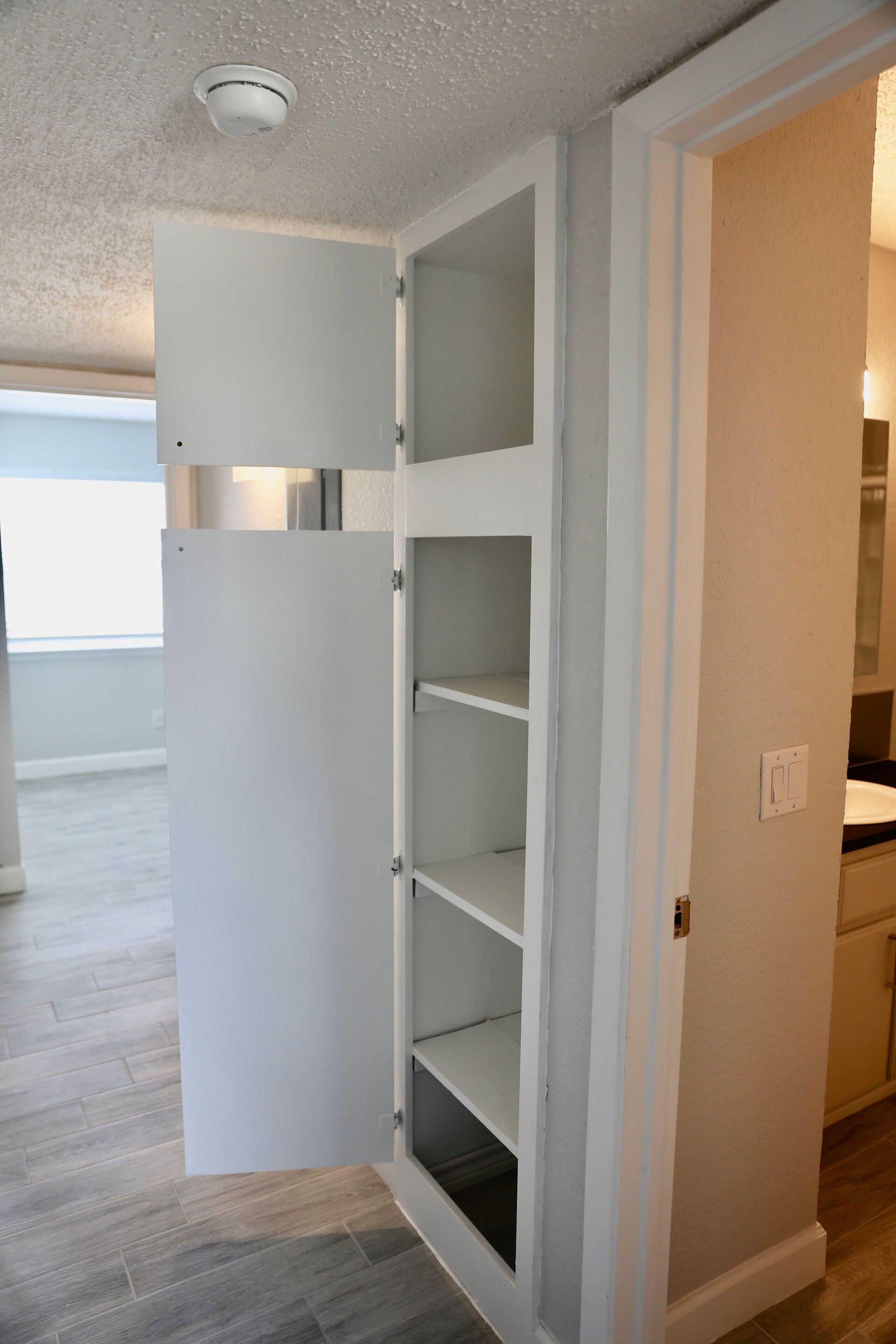 A white cabinet with shelves in a hallway next to a bathroom.