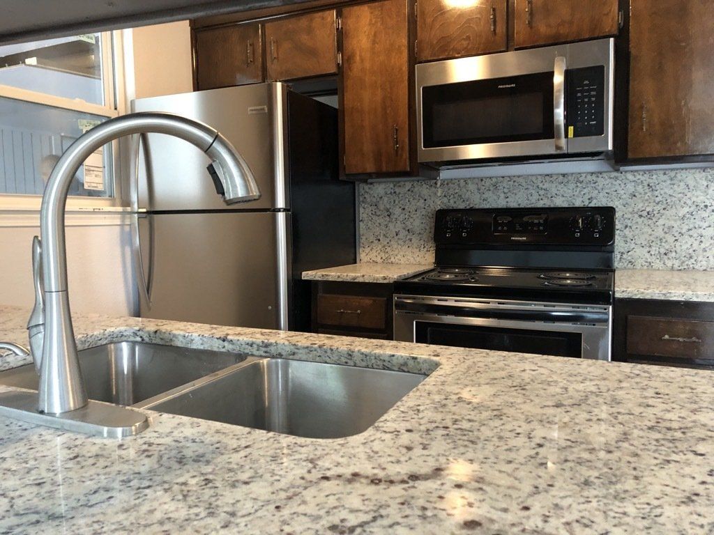 A kitchen with a sink , stove , refrigerator and microwave.