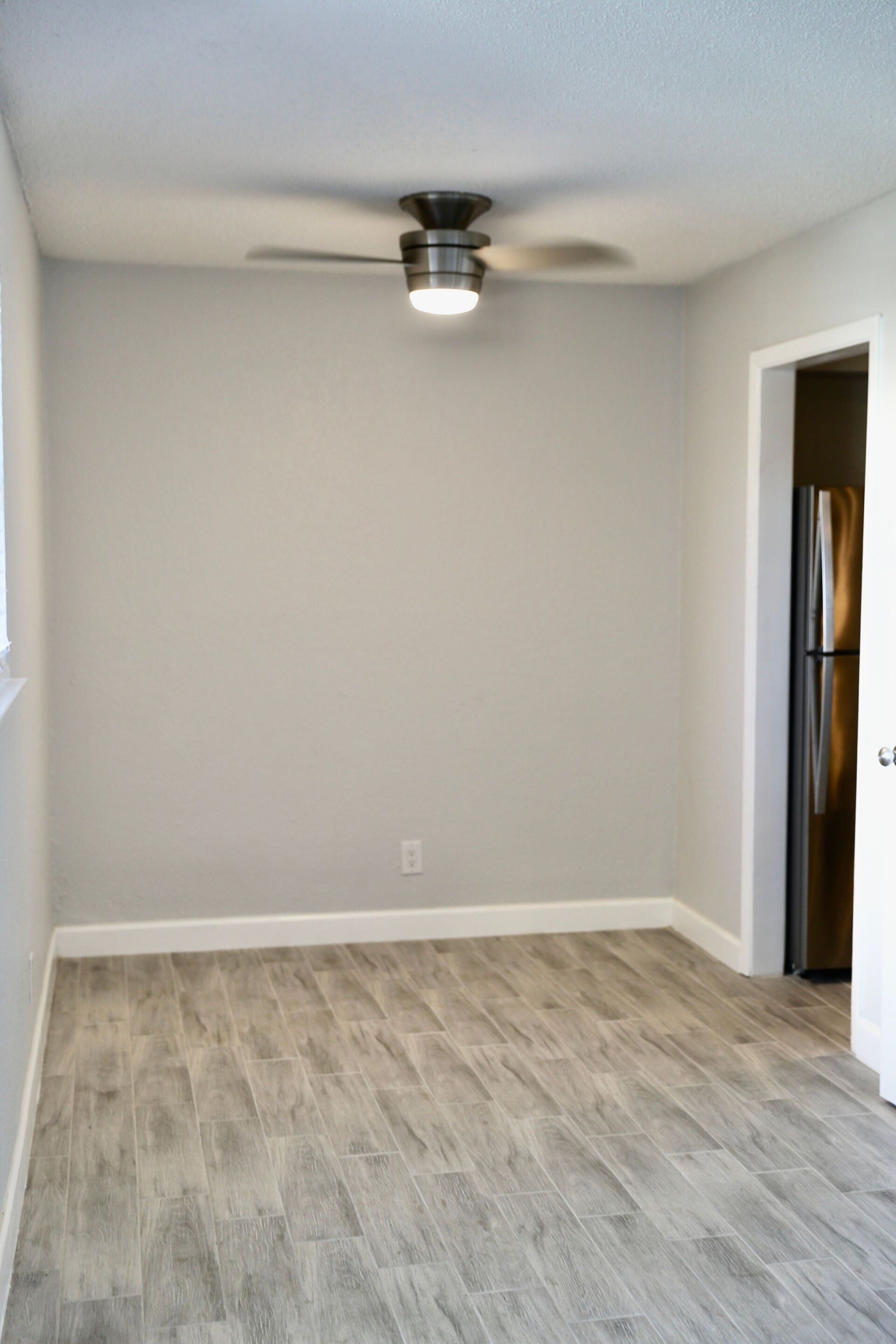 An empty room with a ceiling fan and a refrigerator.