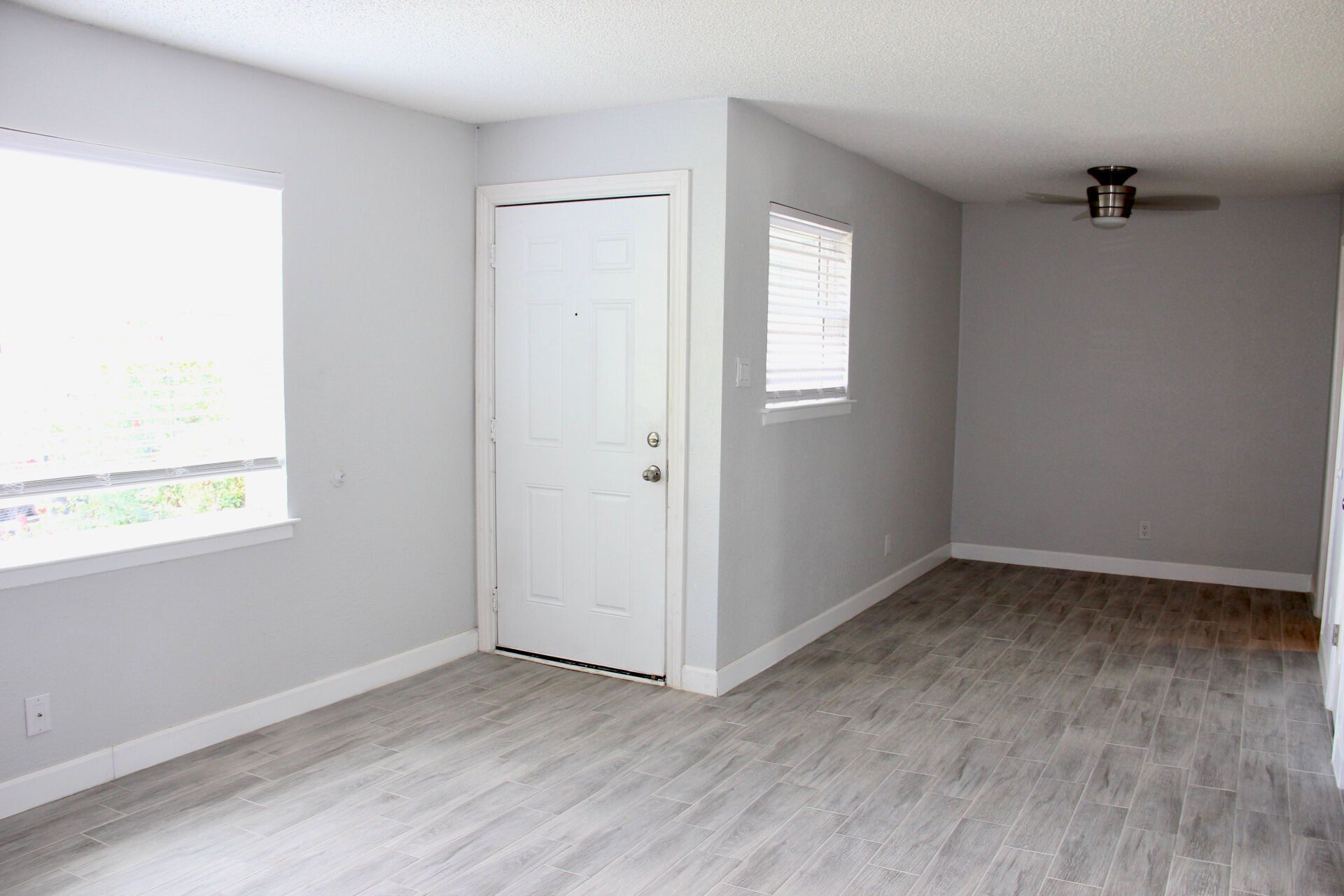 An empty living room with a door , window and ceiling fan.