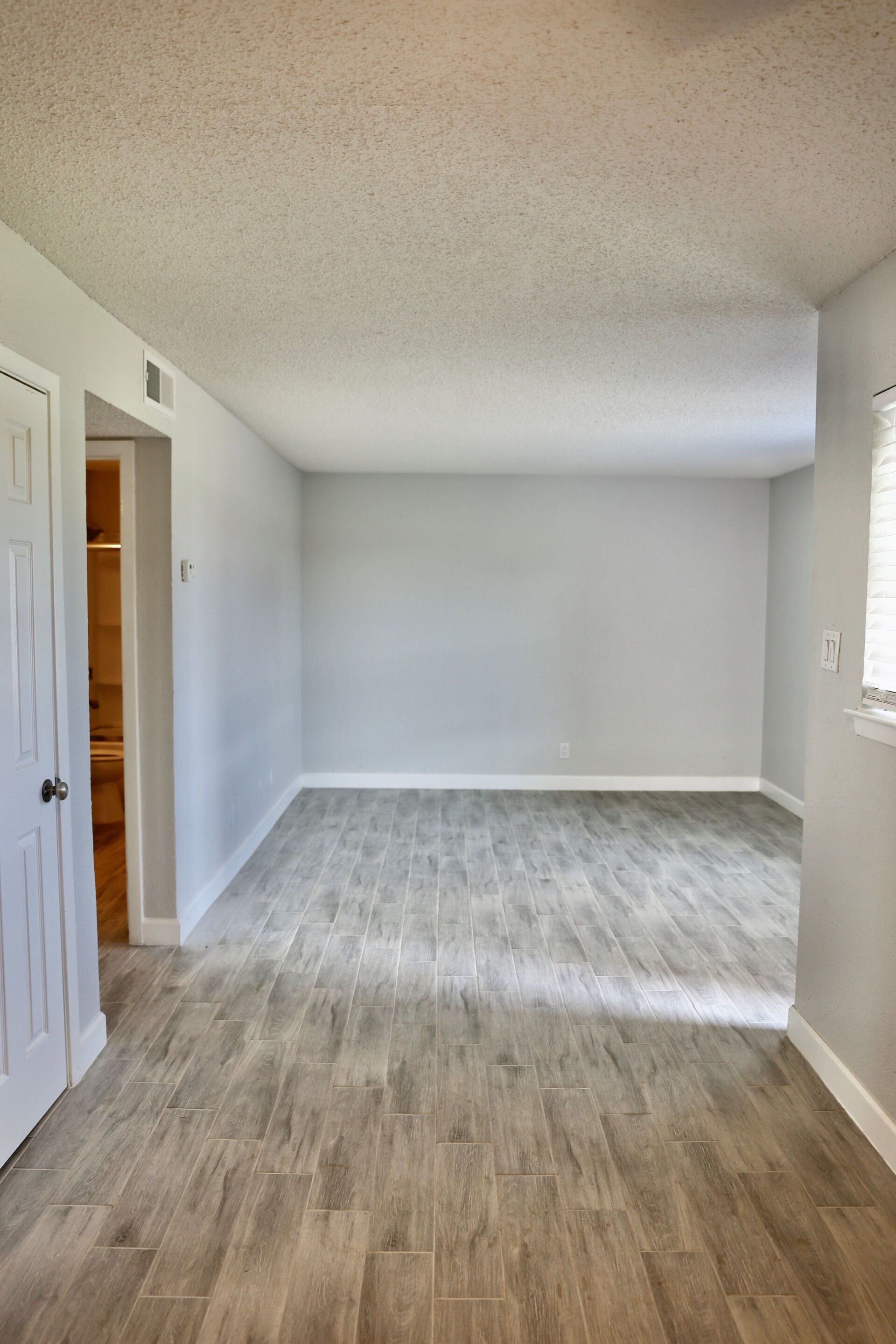An empty living room with a wooden floor and white walls.