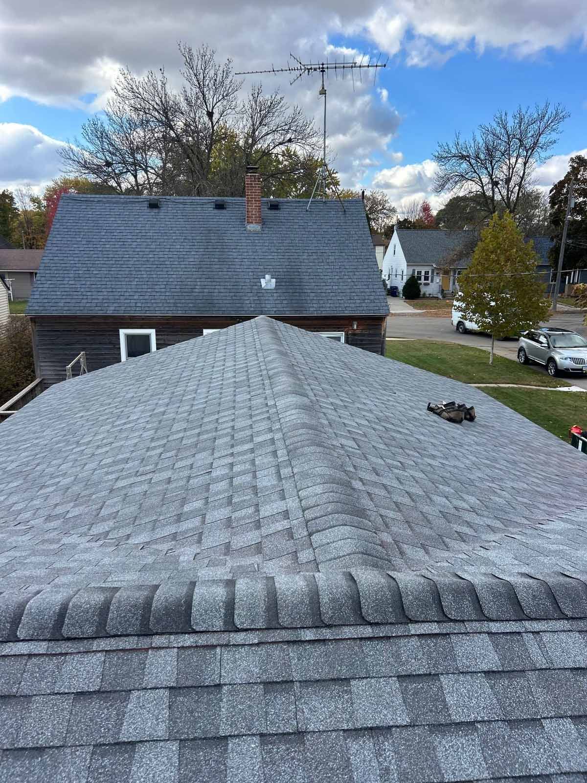 Gray asphalt shingle roof with a ridge, viewed from above, with other houses and trees in the background.