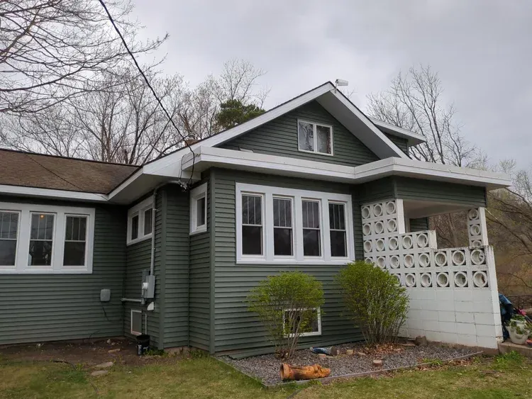Green house with white trim, under a cloudy sky.