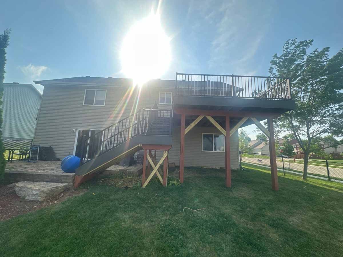 Backyard with a wooden deck attached to a two-story house, sunny day, blue sky, green grass.