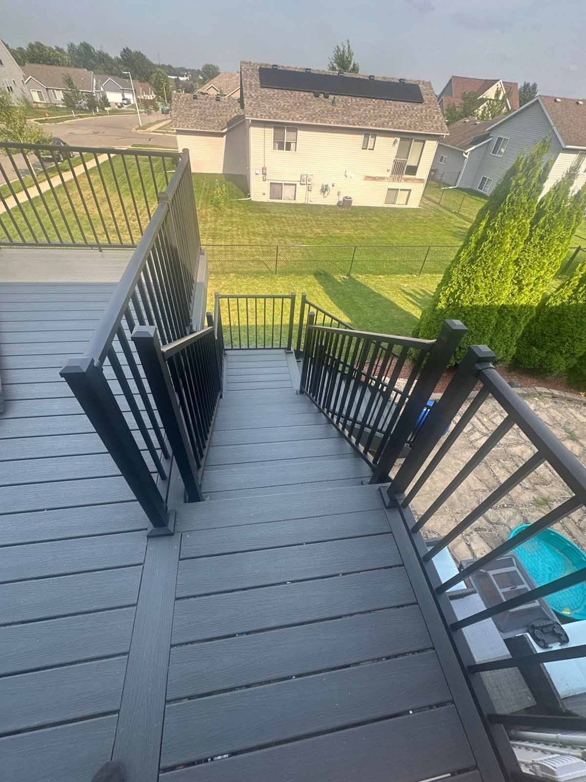 Deck with dark gray steps and black railings, overlooking a yard and houses.