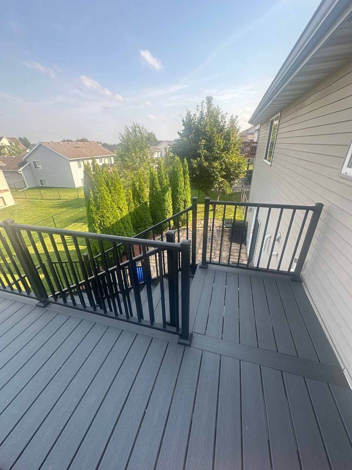 Deck with gray composite boards, black railing, and access gate; house exterior visible.
