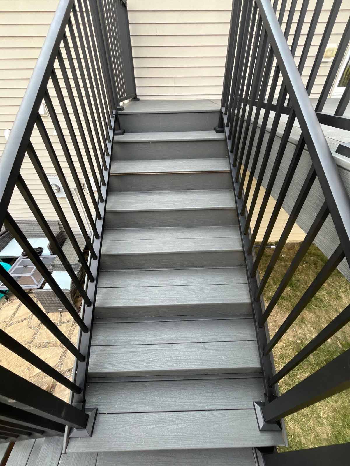 Gray wooden stairs with black metal railings leading up to a beige siding wall.