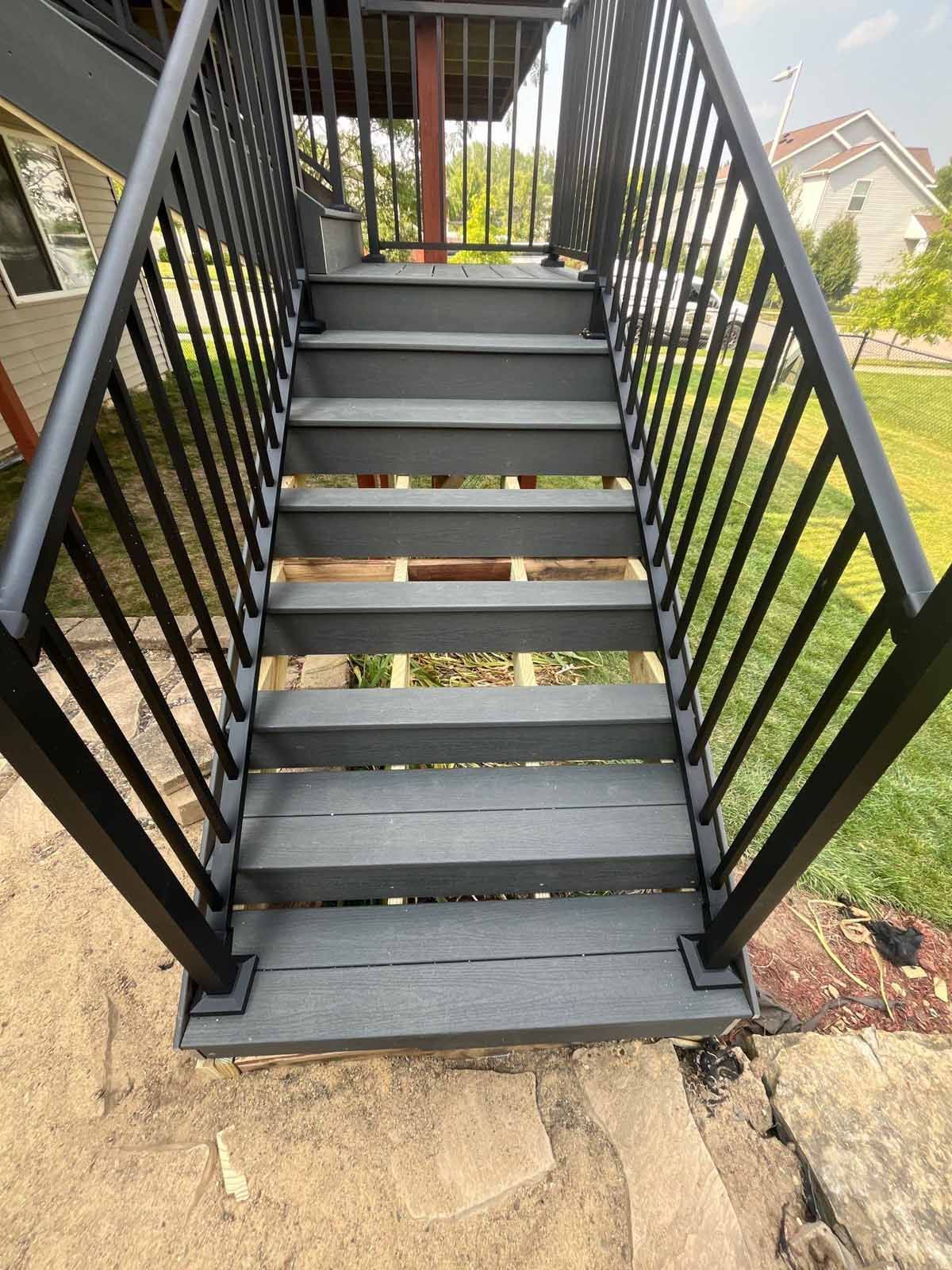 Black stair railing with gray steps leading up from a yard.