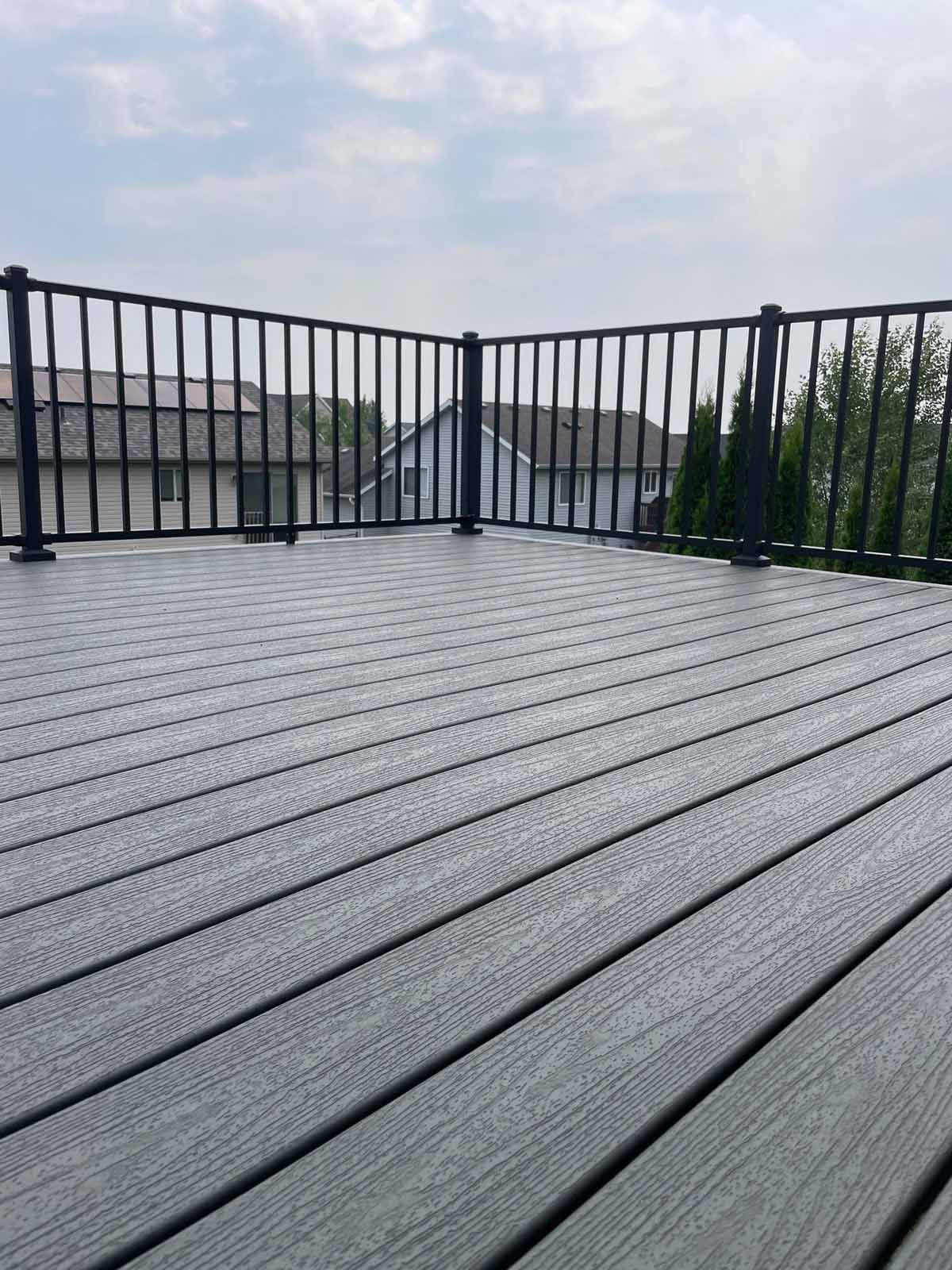 Gray composite deck with black railing overlooking houses under a cloudy sky.