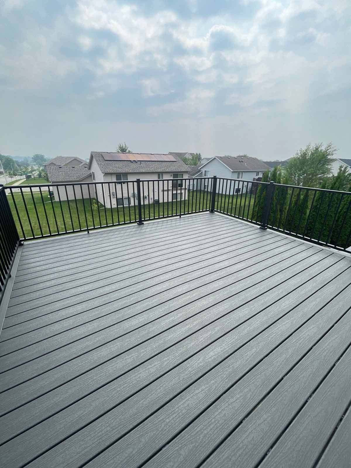 Gray composite deck with black railing overlooking a residential neighborhood under a cloudy sky.