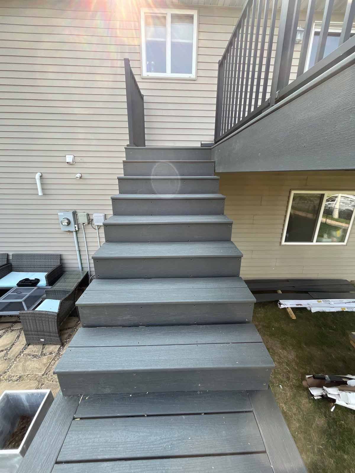 Grey composite stairs leading up to a deck, against a beige house wall.