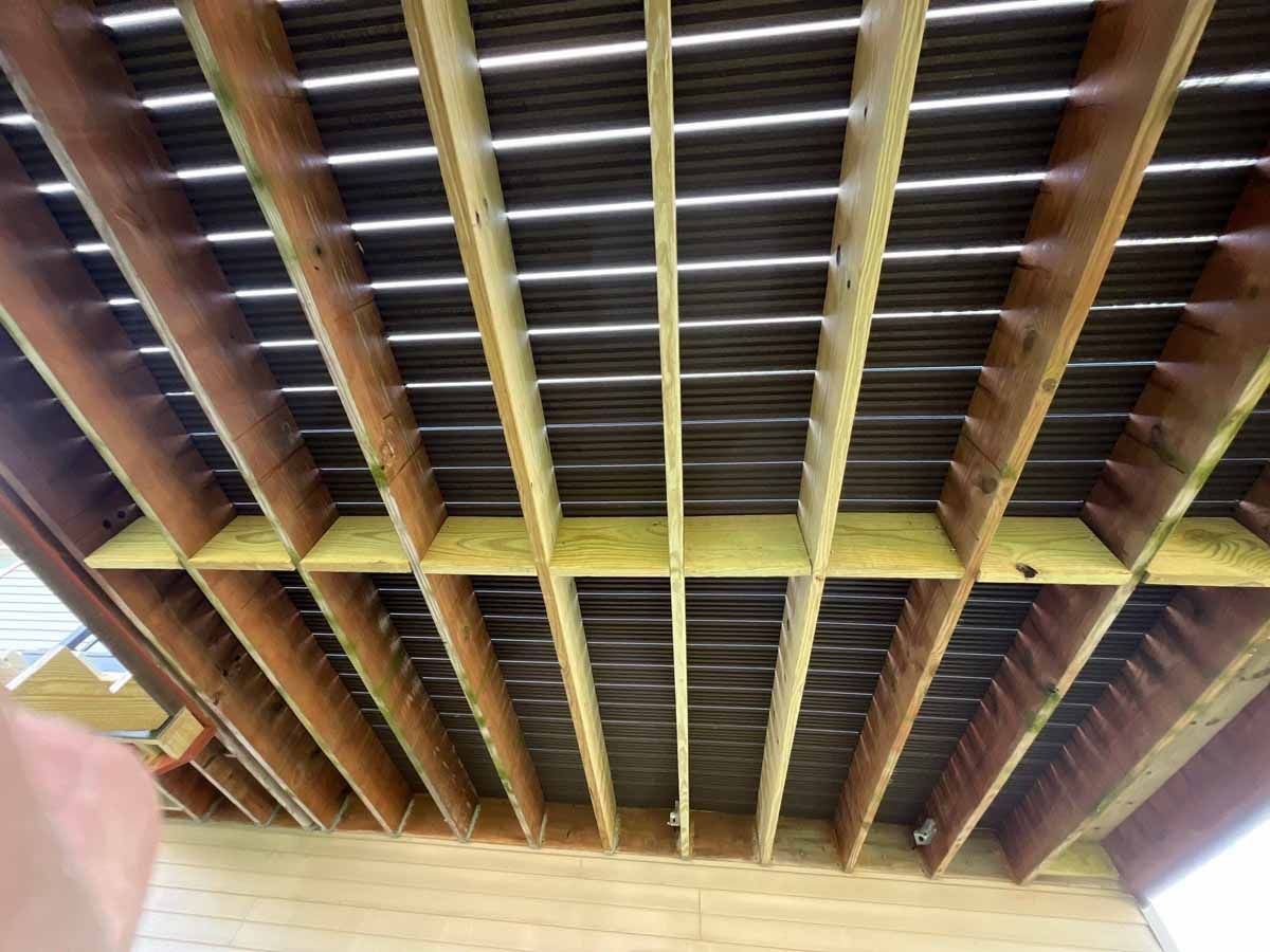 View from below of a wooden deck frame, showing joists and support beams, with a dark surface above.