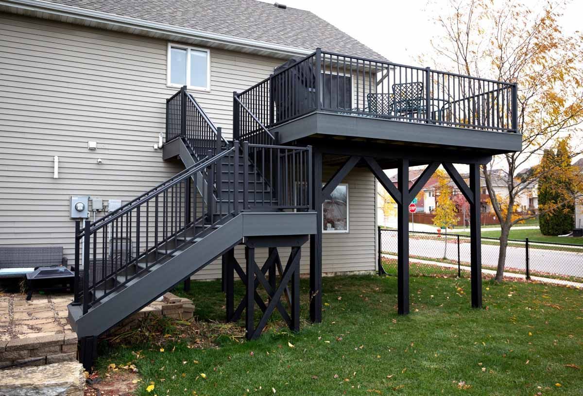 Family on a deck, with a table and chairs, near a modern house with large windows.