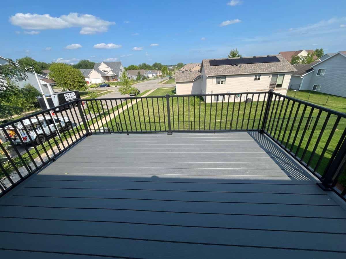 Gray deck with black railing overlooking a suburban neighborhood on a sunny day.