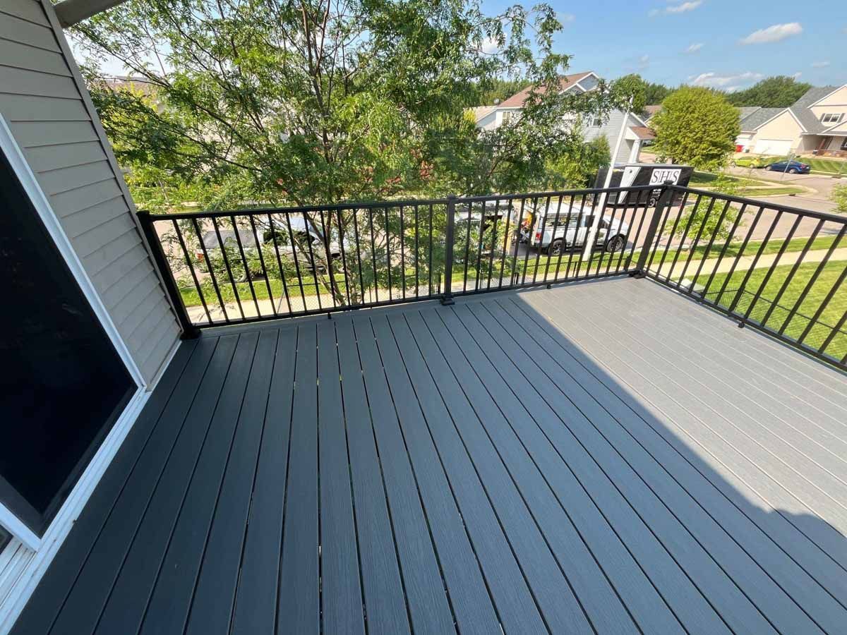 Deck with black railing overlooking a yard with houses and trees. Deck boards are gray.