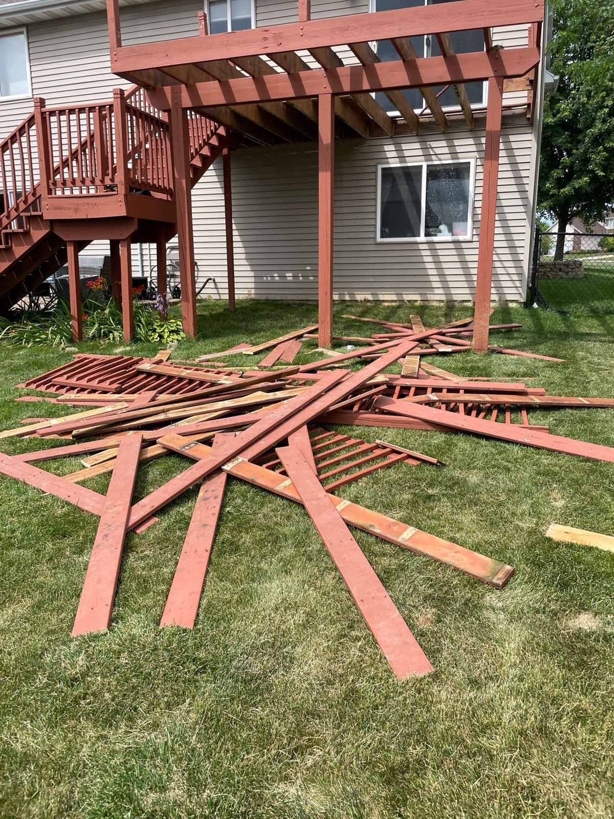 Pile of reddish-brown wooden slats and lattice on green grass in front of a house and deck.