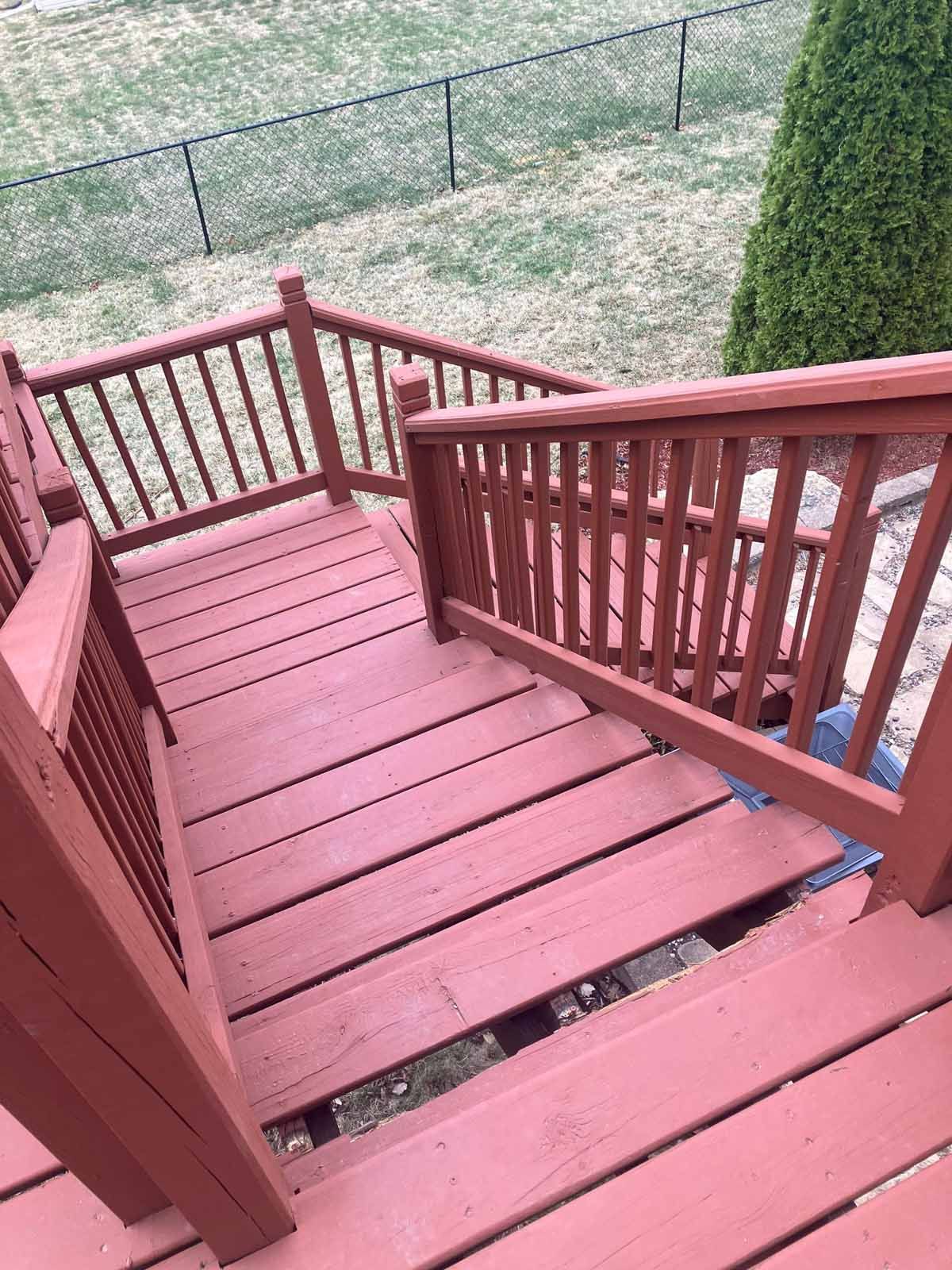 Red painted wooden deck and stairs leading down to a yard, with handrails on either side.