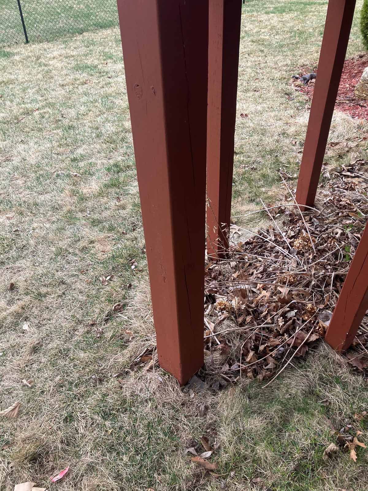 Brown wooden deck supports in a grassy yard, surrounded by dead leaves.