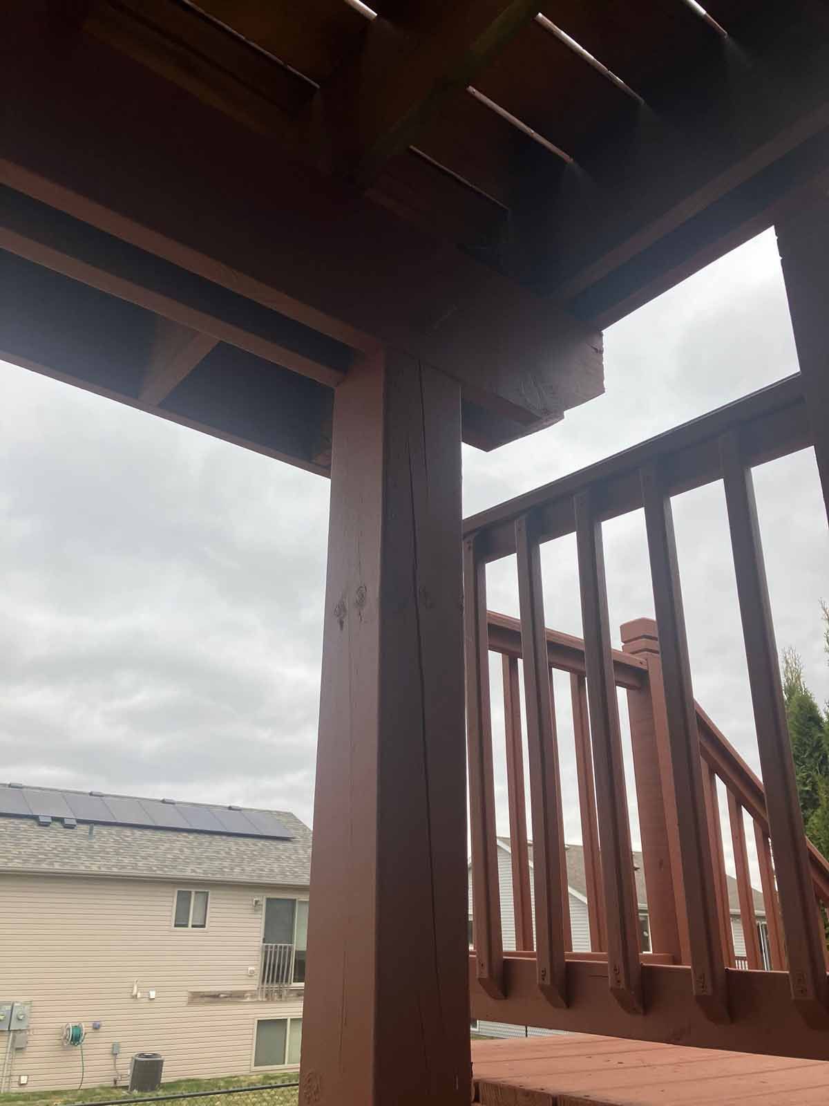Brown deck post and railing, cloudy sky visible, house with solar panels in background.