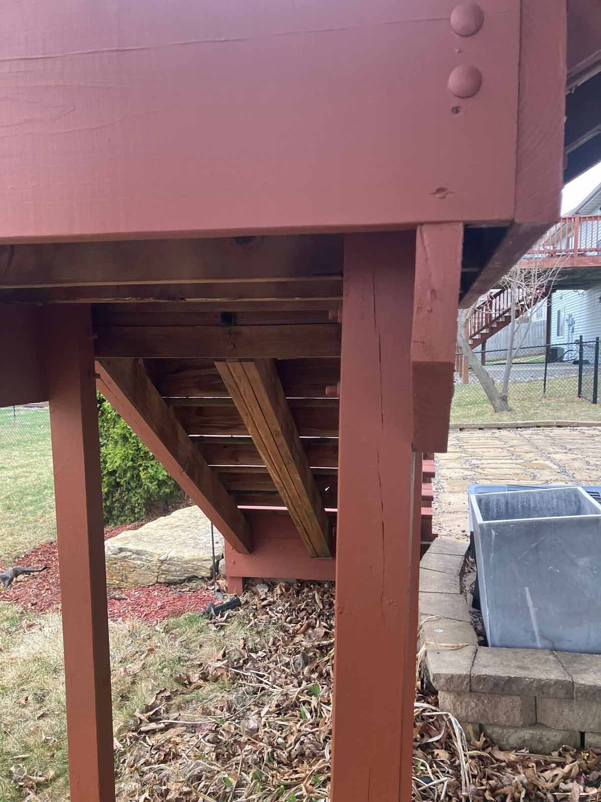 Red-painted wooden deck with steps, supported by posts. The deck overlooks a yard with grass and a stone patio.