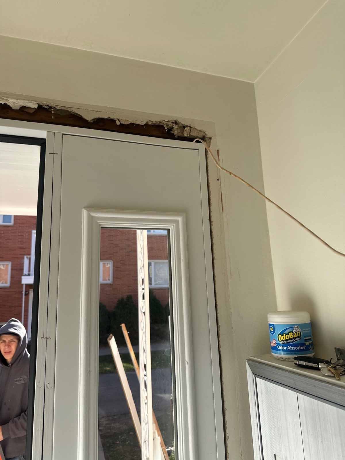 A person standing near a white door with a window, construction debris, and a can of sealant.