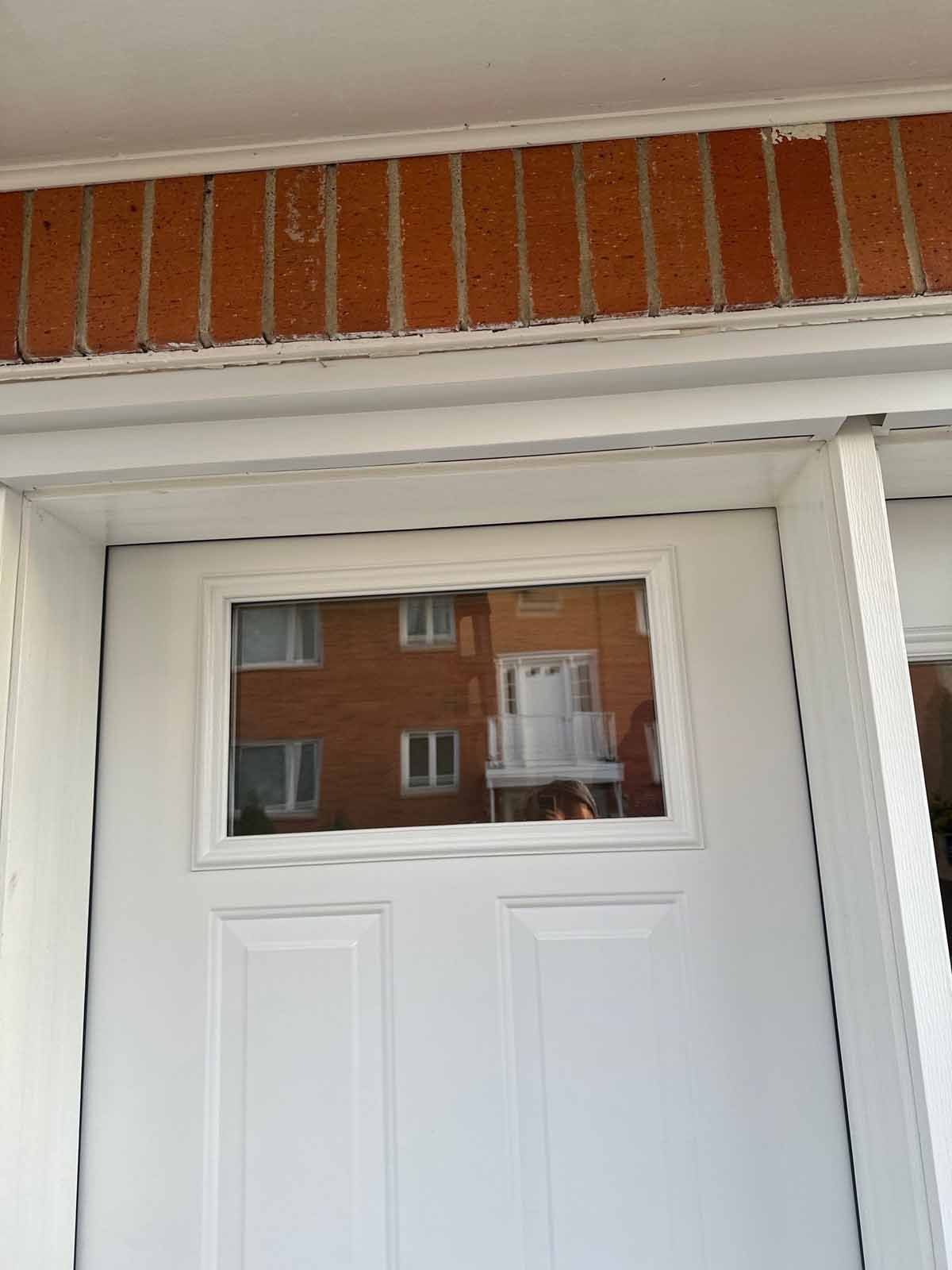 White door with rectangular glass window reflecting a brick building.