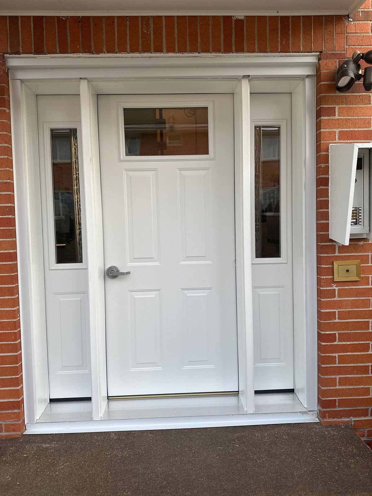 White front door with sidelights, set in brick. A mailbox and security light are visible.