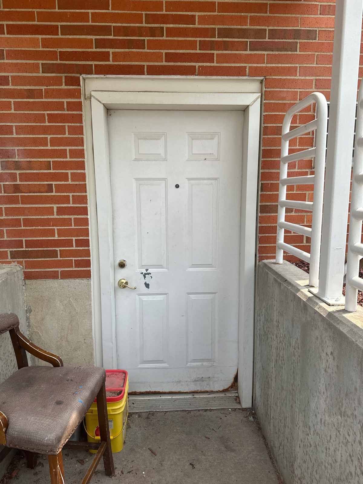 White door set in a brick wall. A chair and railing are nearby.