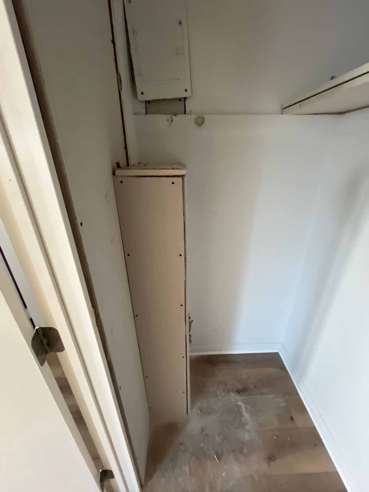 A narrow closet interior with a tall, thin built-in cabinet. Beige walls and a wooden floor are visible.