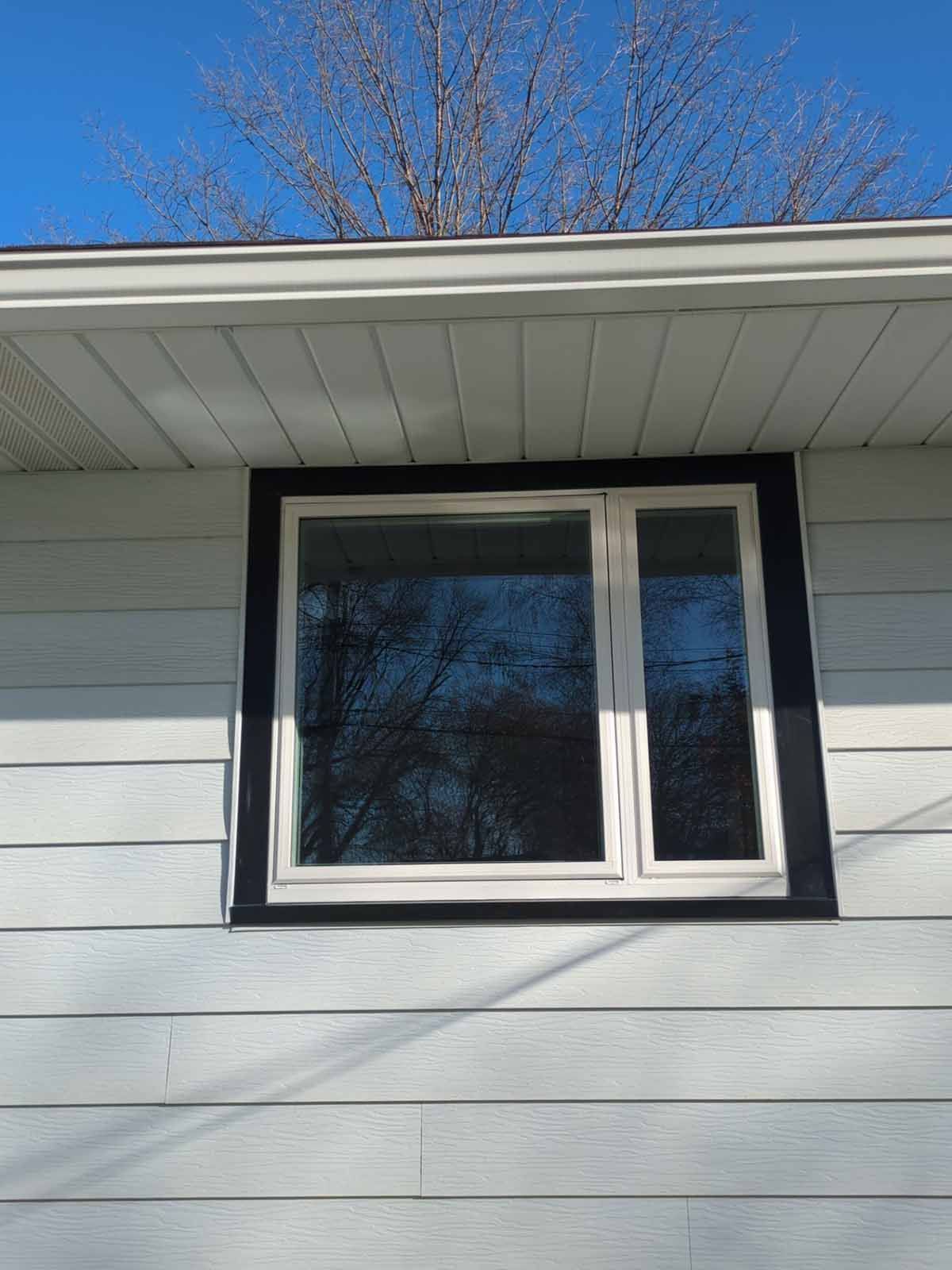 Window with white frame and black trim on a light blue-sided house under a clear sky.