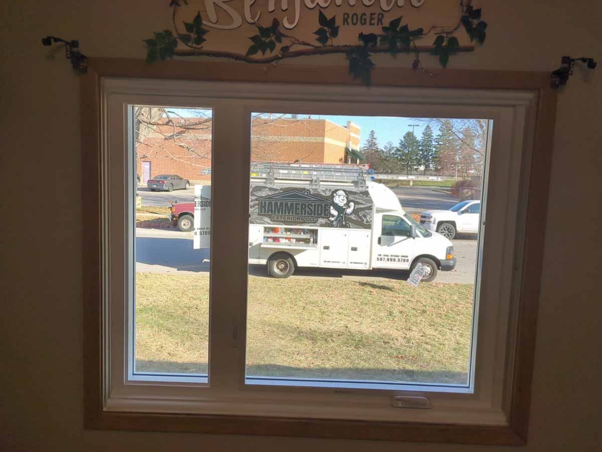 Two-story house with cream siding and black shutters. Windows are white-framed. Landscaping includes rocks and grass.