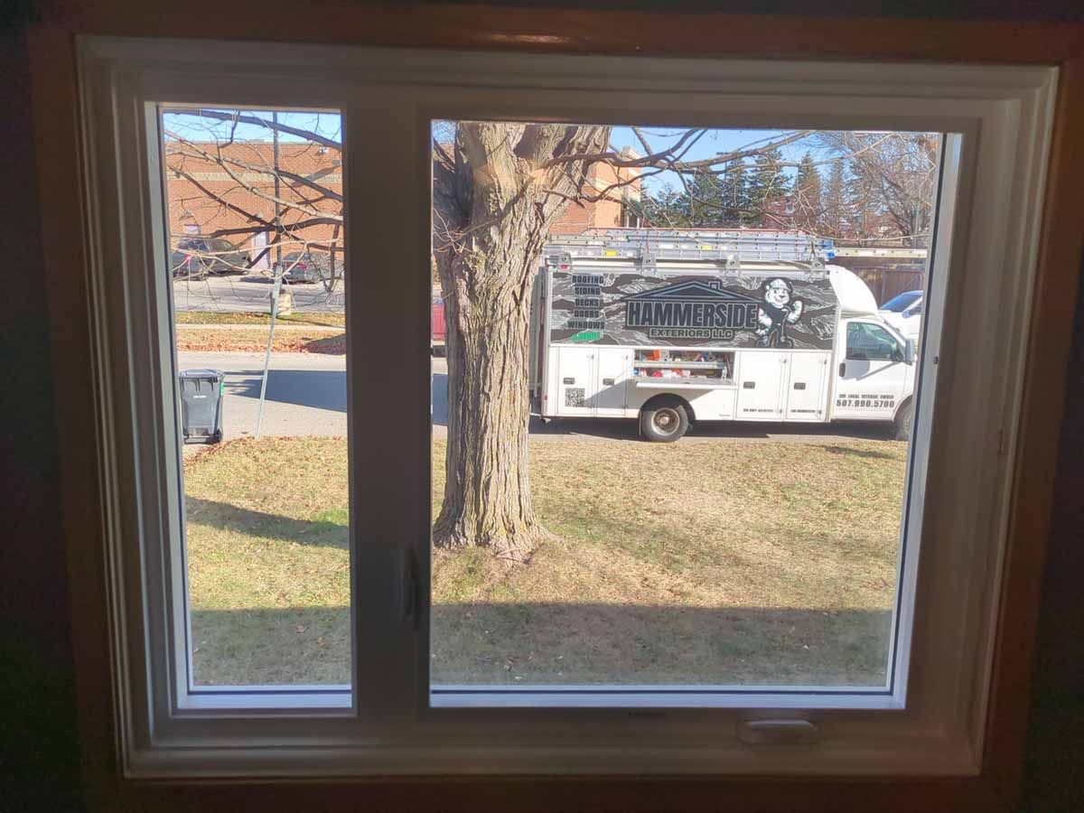 Window looking out at a grassy yard, tree, and white service truck.