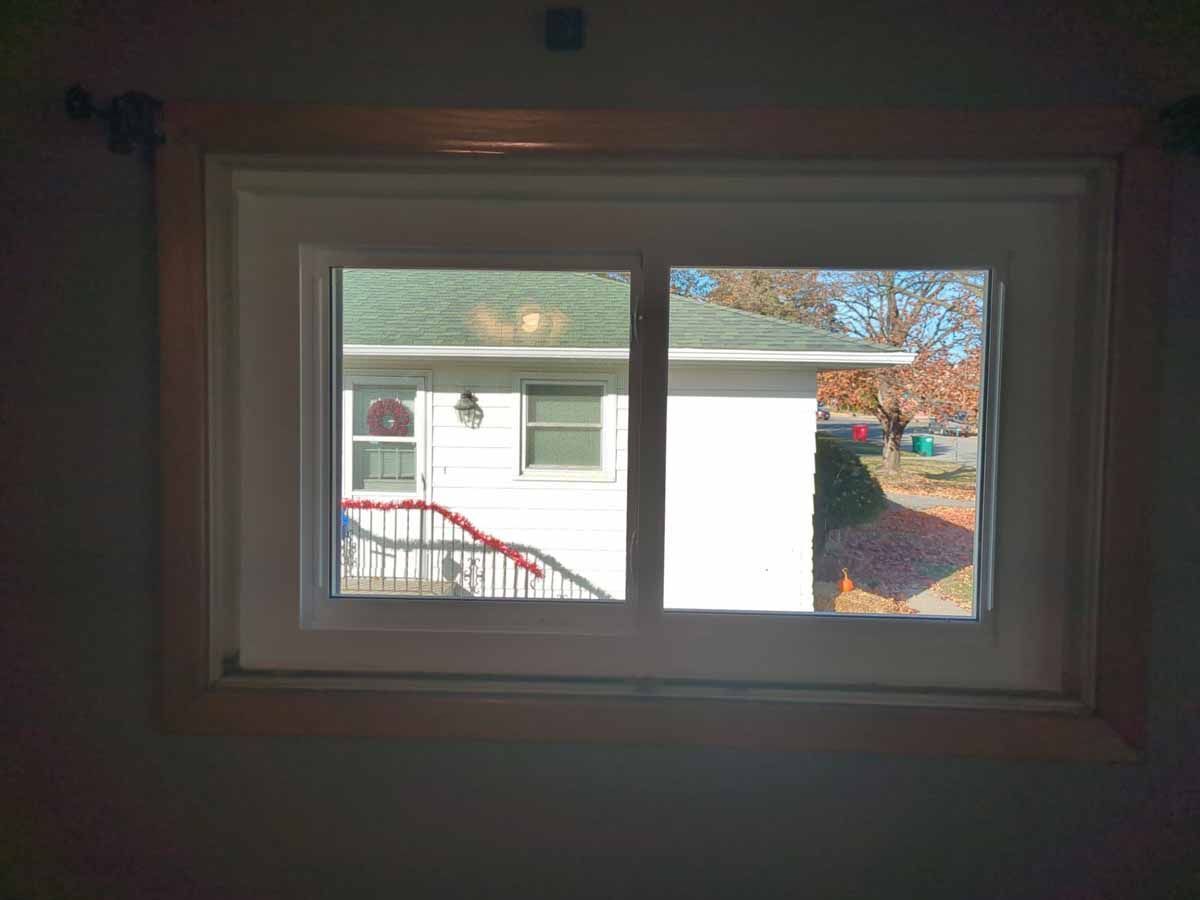 Window framing a view of a white house with red railing and trees with fall foliage.