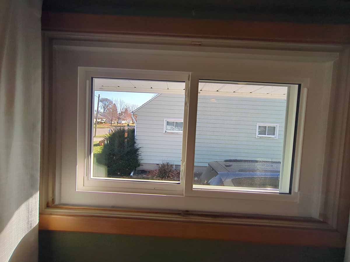 Two-pane window with a view of a house and yard. Bright daylight illuminates the scene.