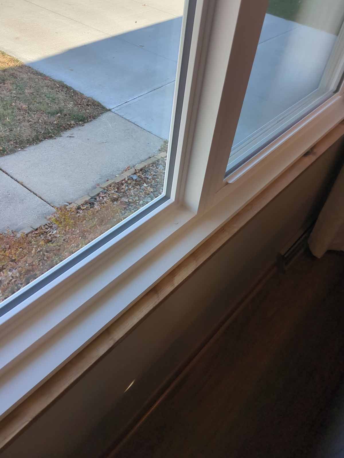 Window with white frame, overlooking a sidewalk and grass. Brown wall and wood trim below the window.