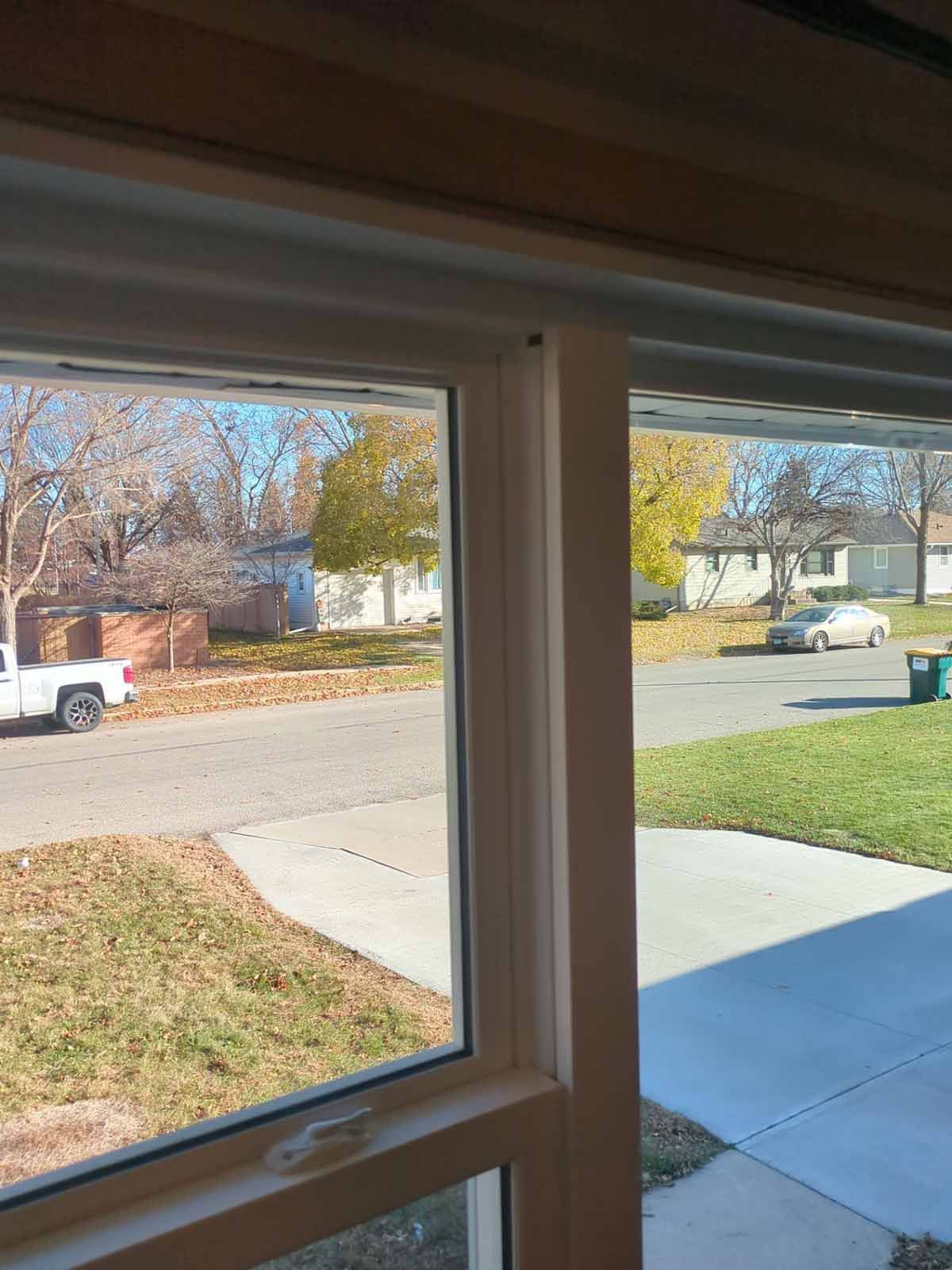 View through a window of a suburban street with houses, trees, a truck, and a car.