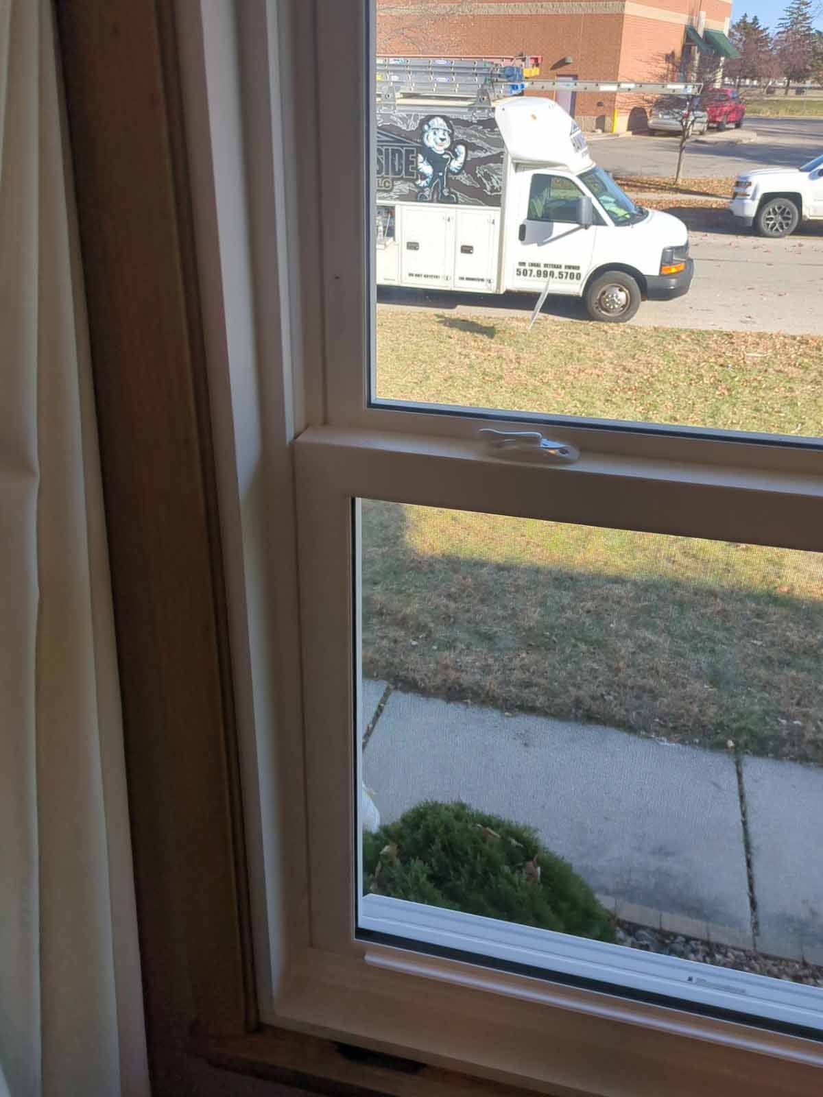 Window view: white paneled window frame, outdoors, white work truck, grass and sidewalk.