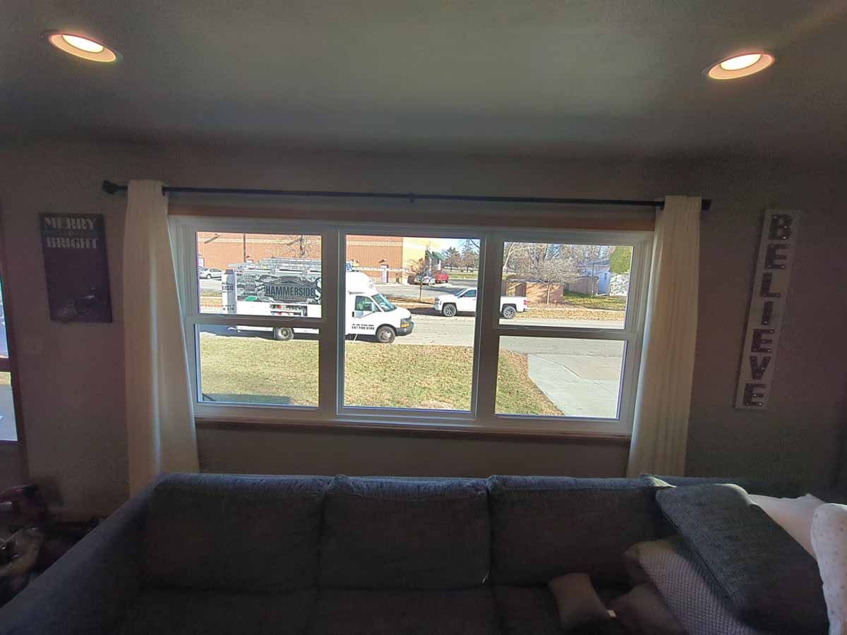 A living room with a large window overlooking a street with vehicles. A gray couch sits in the foreground.