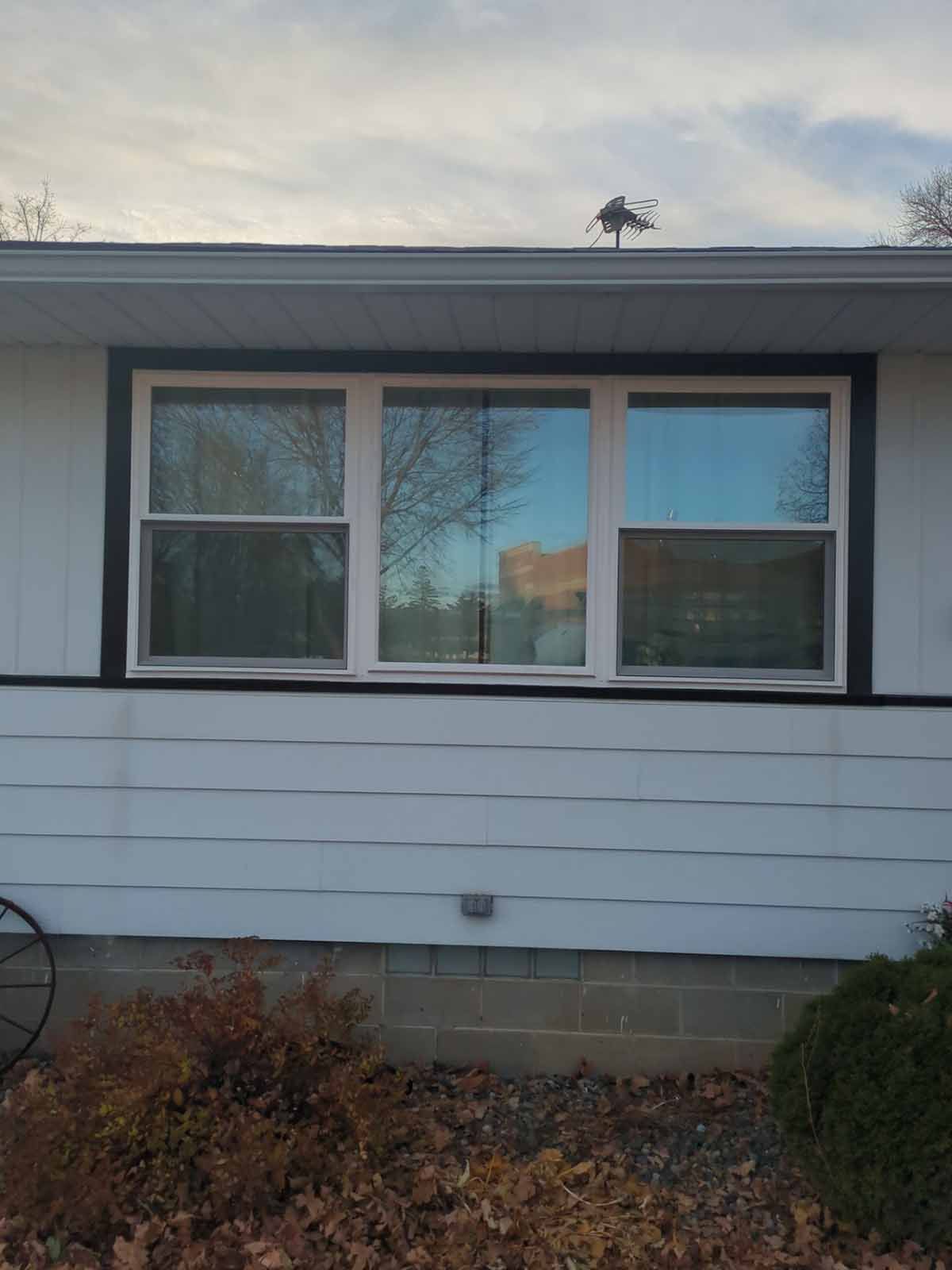Three white-framed windows with black trim on a white house, set against a cloudy sky.