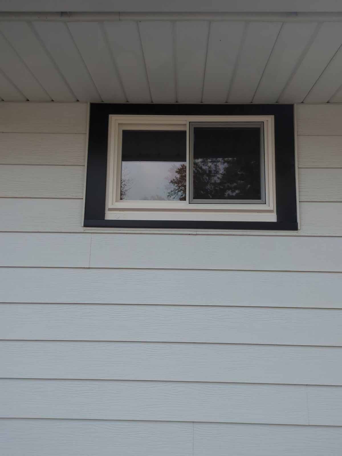 Black-framed window on a light blue siding house, with a white window frame and dark shades inside.
