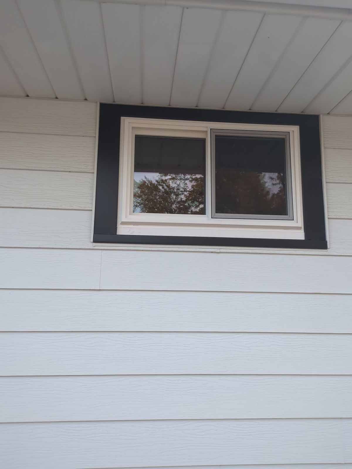 White house siding with a window framed by black and white trim.