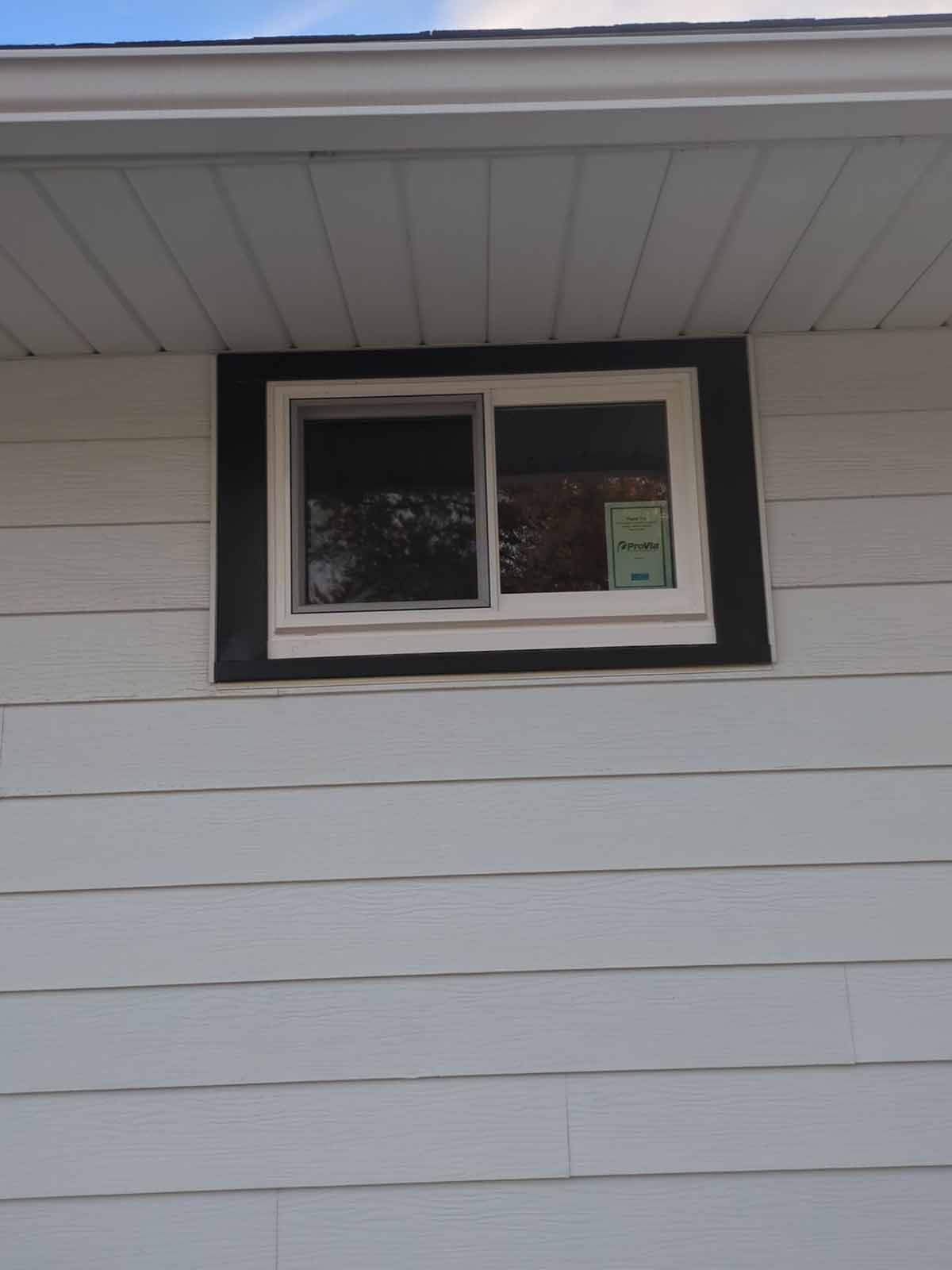 White siding with a window framed by black trim. The window is white.