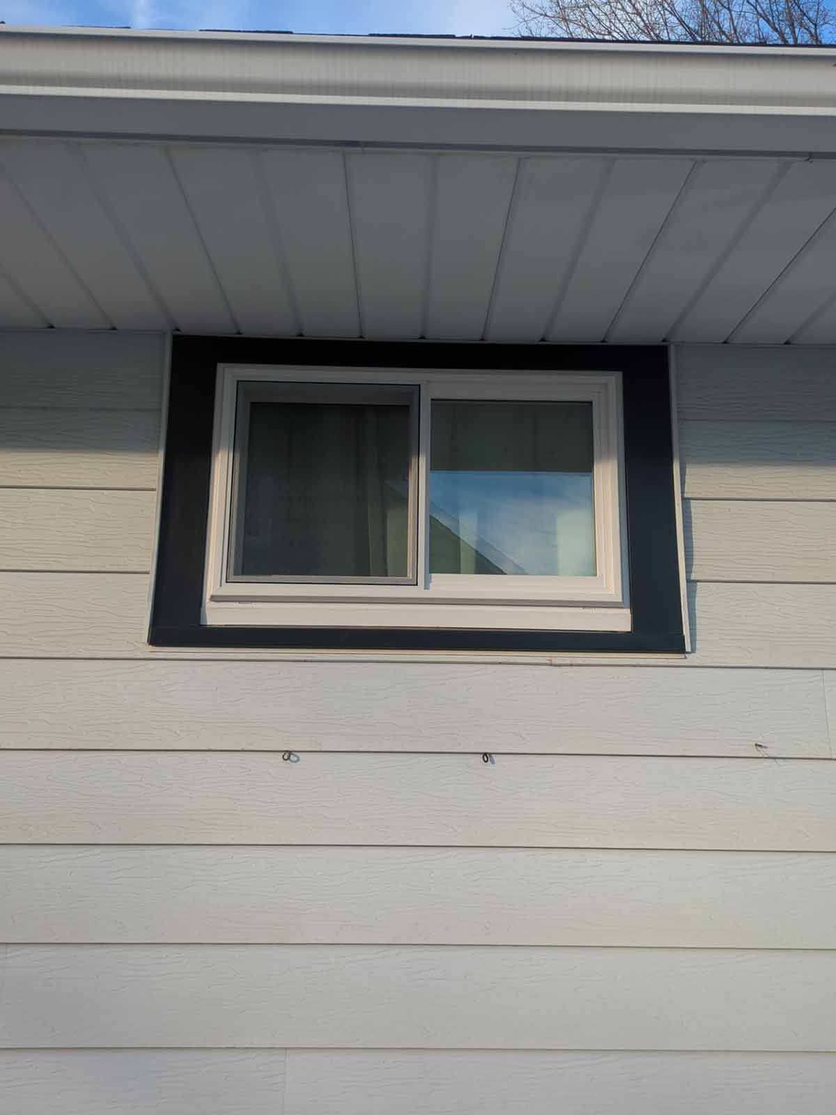 A white framed window with black trim, set into a light gray house siding.
