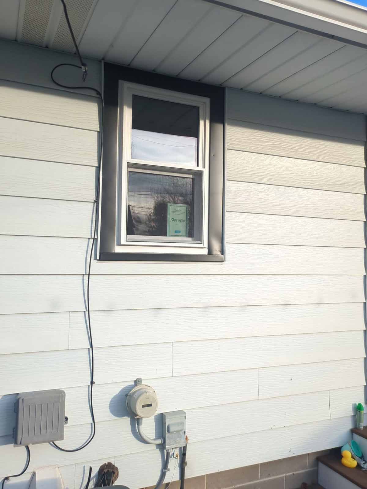 Window on a house with gray siding, black trim. Utility boxes and cable on the wall.