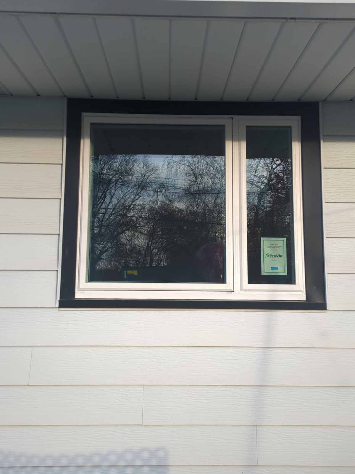 White window framed with black trim on a light gray clapboard house.