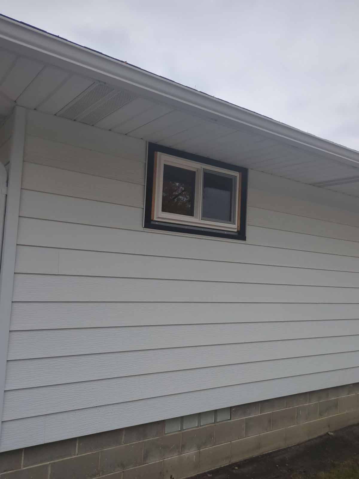 White siding on a building with a window surrounded by a dark frame and a white trim.