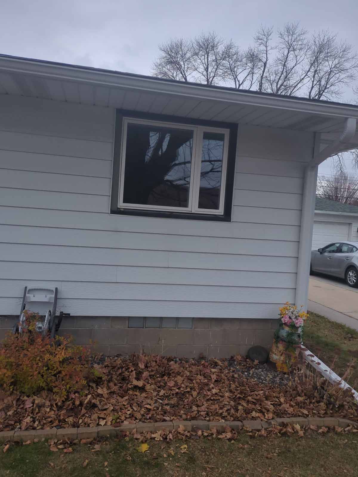 White house exterior with window and brown trim. Brown leaves and a small ladder sit below.