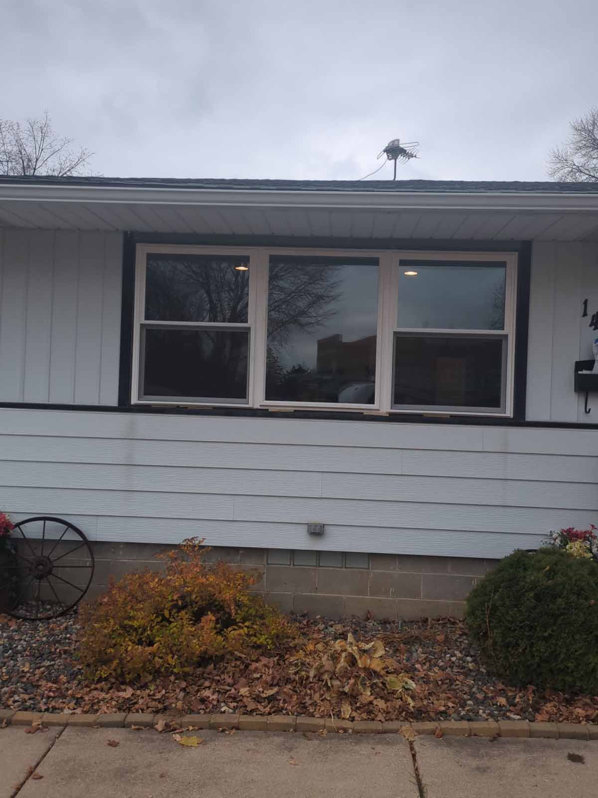 A house with a large three-pane window framed by black and white trim. Bushes and plants are below.