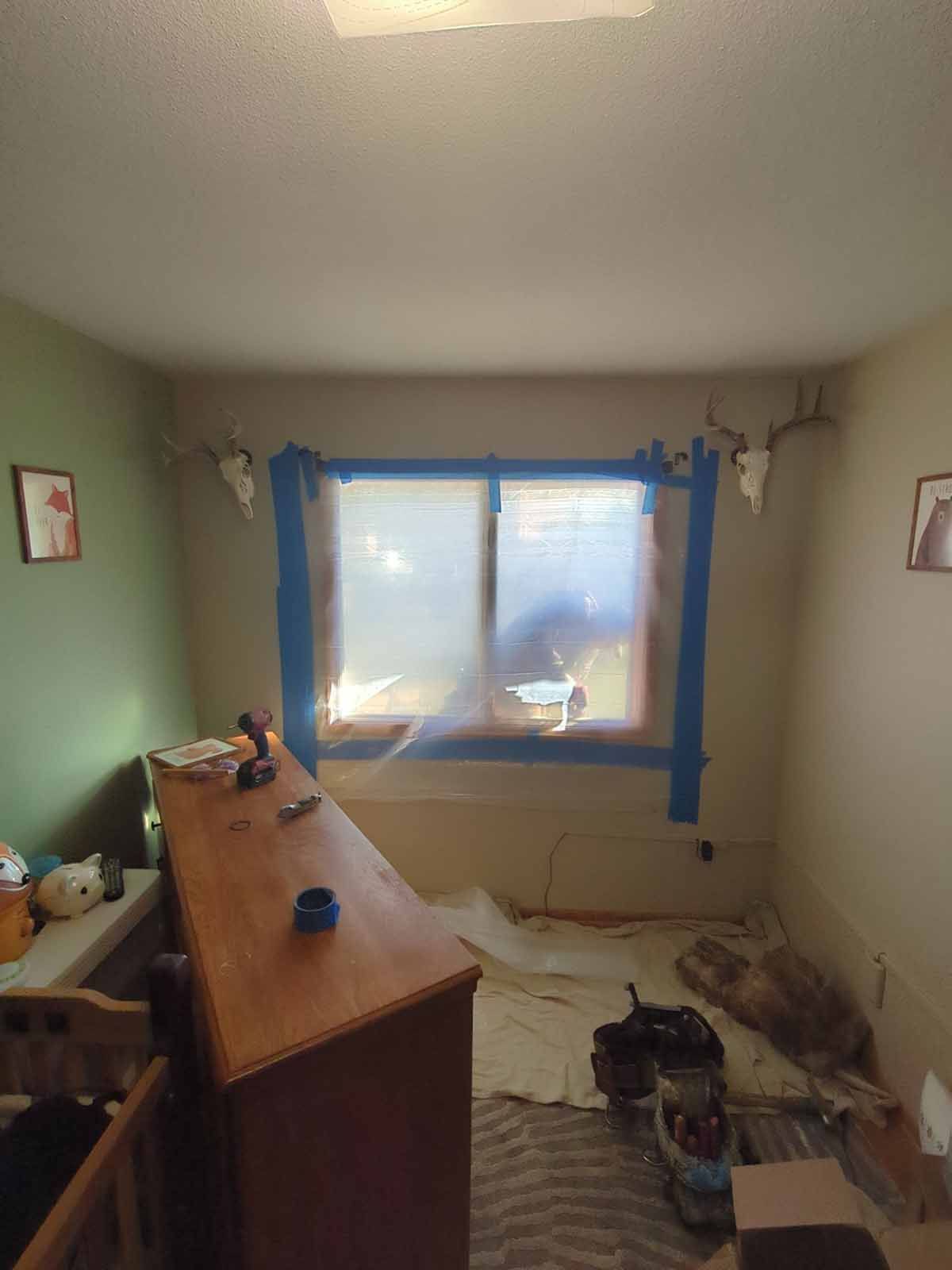 Room with a window taped off for painting, a dresser, and deer antlers on the walls.