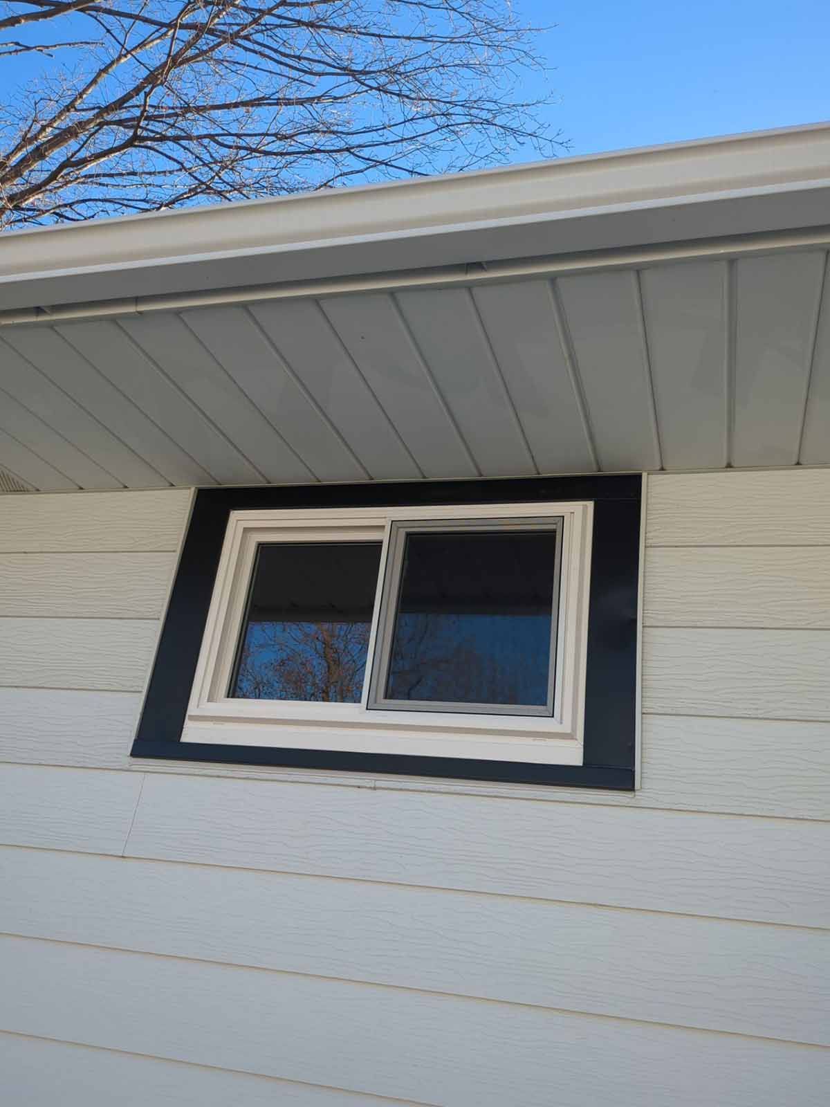 Exterior view of a white-sided building with a window framed in black trim, under white eaves.